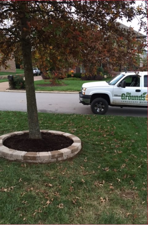 Grass with stone planter and tree with the Ground Guys truck