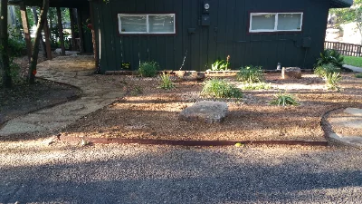 dirt yard with bushes, rocks and stone walkway in front of house