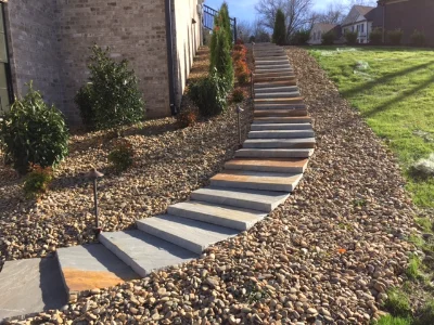 stone steps lined by rocks with trees and bushes leading to house.