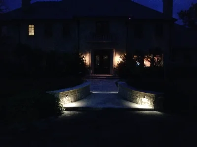 stone walkway and short walls leading to house lit in the night.