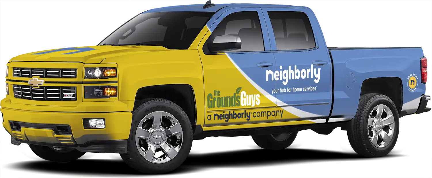 The Grounds Guys service truck with yellow company wrap and blue Neighborly wrap.