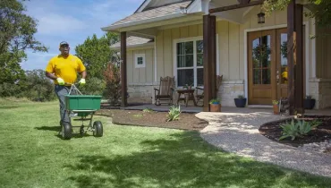 The Grounds Guys service professional fertilizing a homeowner's front lawn.