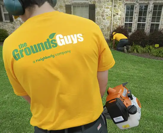 Grounds Guys employee wearing branded t-shirt and using leaf blower to clean up client's front yard.
