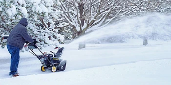 Man using a snow blower in wintry conditions.