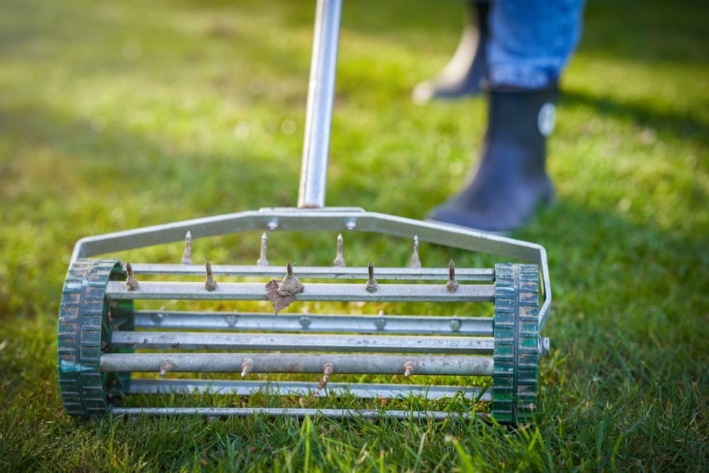 Landscaper using lawn aeration tool on grass.