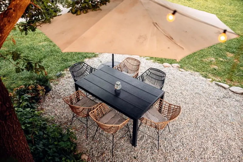 Dining table and chairs on top of pea gravel in a backyard.