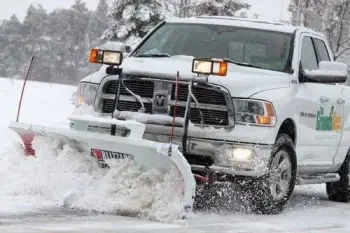 The Grounds Guys white snow plow hauling snow on a rural residential street.